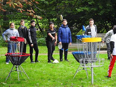 Jugendliche spielen Discgolf an bunten Körben