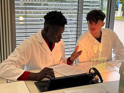 Zwei Schüler in Laborkitteln besprechen einen Versuch mit Reagenzgläsern