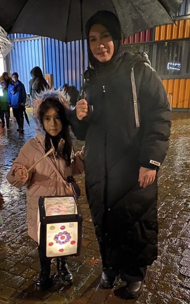 Mädchen mit Laterne und Mutter mit Regenschirm beim Laternenumzug im Regen