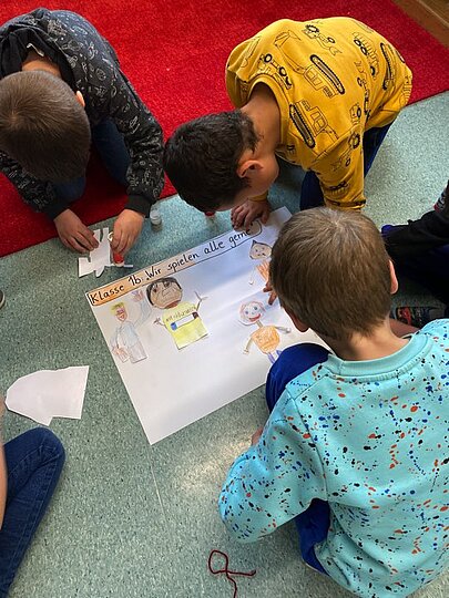 Grundschulkinder gestalten auf dem Boden gemeinsam ein Plakat