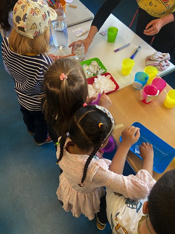 Kinder experimentieren mit bunten Bechern und Wasser am Tisch