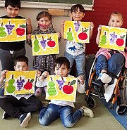 Vorschulkinder zeigen ihre gedruckten Obstbilder mit Birnen, Trauben und Äpfeln