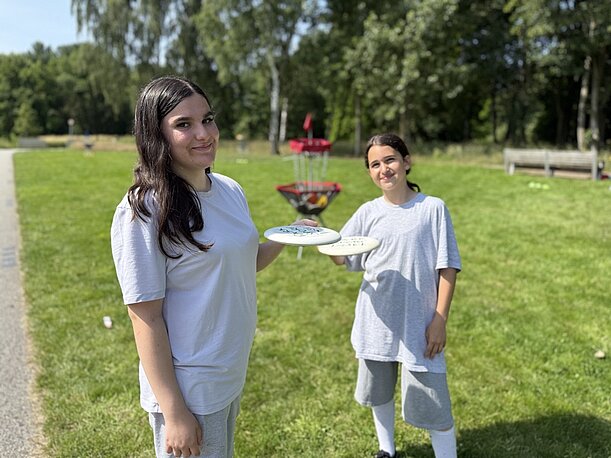 Maryam und Esma mit Frisbeescheiben an einem Discgolf-Korb