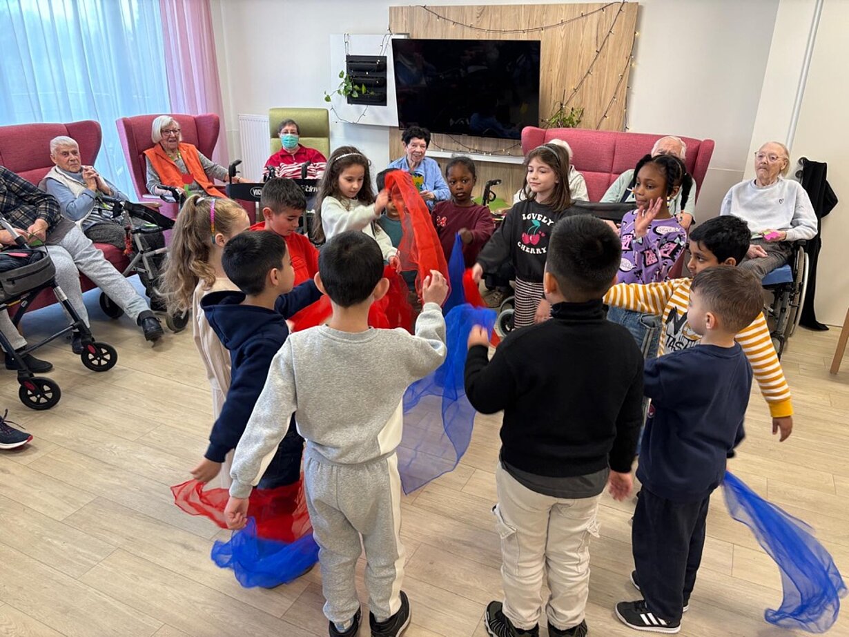 Vorschulkinder tanzen mit Tüchern vor Senioren im Seniorenheim
