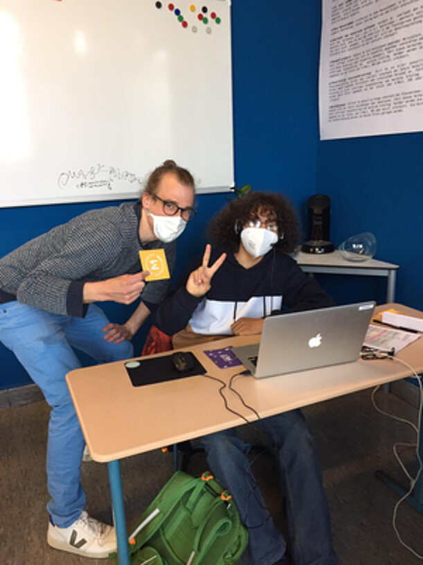 Zwei Personen mit Masken am Laptop zeigen das Victory-Zeichen