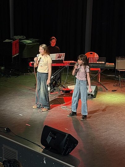 Zwei junge Sängerinnen auf der Bühne vor Band und Lautsprecher