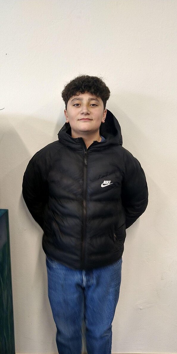 Göktug aus der 8b in schwarzer Steppjacke vor weißer Wand