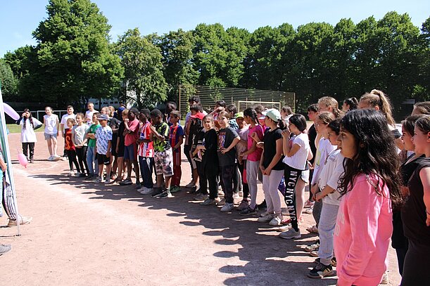 Kinder stehen in einer langen Reihe bei der Siegerehrung auf dem Sportplatz