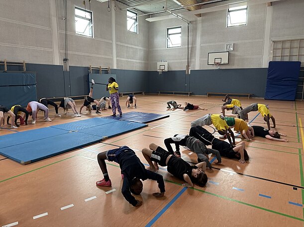 Kinder üben Brücken und Akrobatik auf dem Hallenboden mit der NAFSI-Gruppe