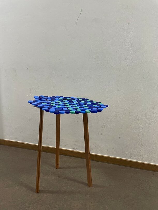 Hocker mit Sitzfläche aus blauen Flaschendeckeln auf Holzbeinen