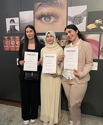 Drei junge Frauen mit Urkunden vor ihren ausgestellten Wettbewerbsfotos