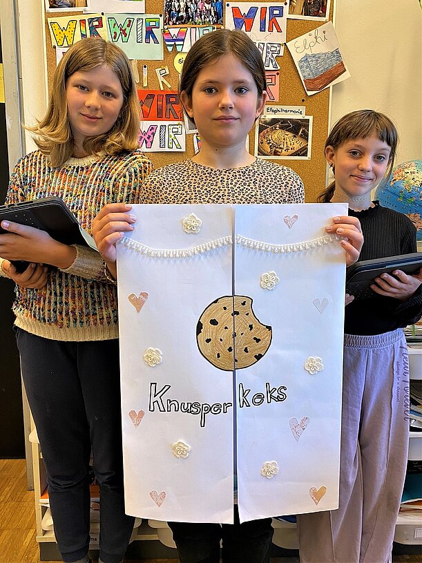 Drei Schülerinnen mit Plakat „Knusperkeks“ beim Projekt Schade Schokolade