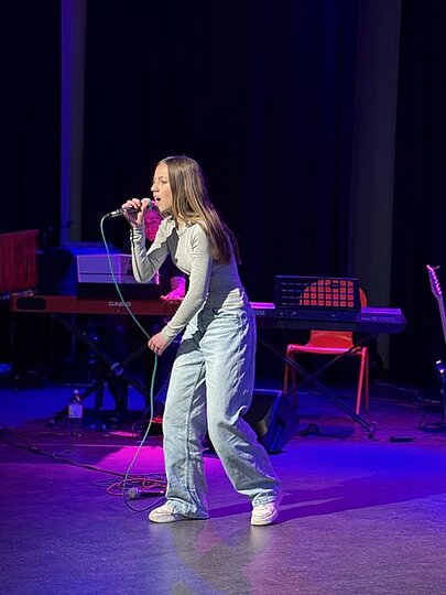 Schülerin in hellen Jeans singt mit Mikrofon auf der Aulabühne