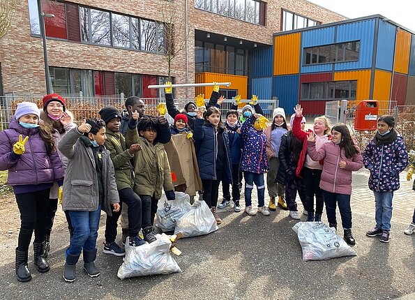 Vorschulklasse mit Müllsäcken beim Frühjahrsputz vor dem Schulgebäude