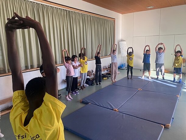 Kinder dehnen sich auf Turnmatten beim Workshop der NAFSI-Tanzgruppe