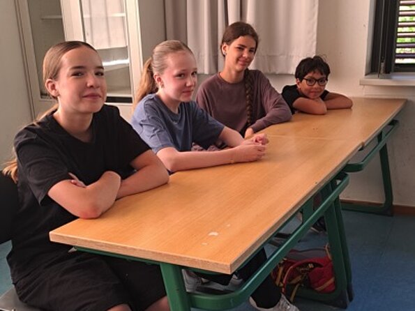 Céleste, Marla, Carlotta und Tyméo an einem Tisch im Klassenraum