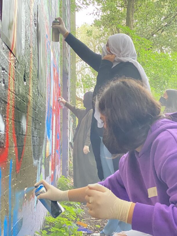 Schülerinnen besprühen eine Wand bei einem Graffiti-Projekt im Freien