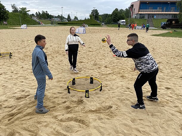 Jugendliche spielen Spikeball auf einem Sandplatz