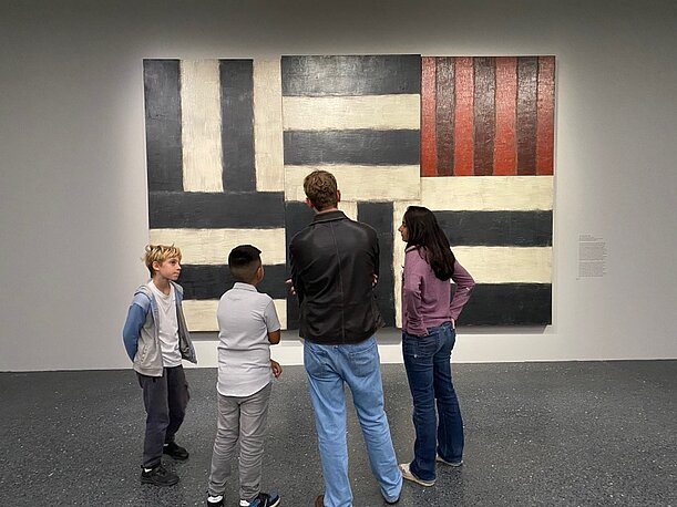 Kinder betrachten mit Begleitpersonen ein Sean-Scully-Gemälde im Museum