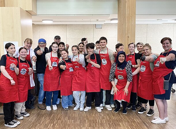 Große Gruppe in roten Schürzen posiert gemeinsam in der Kantine