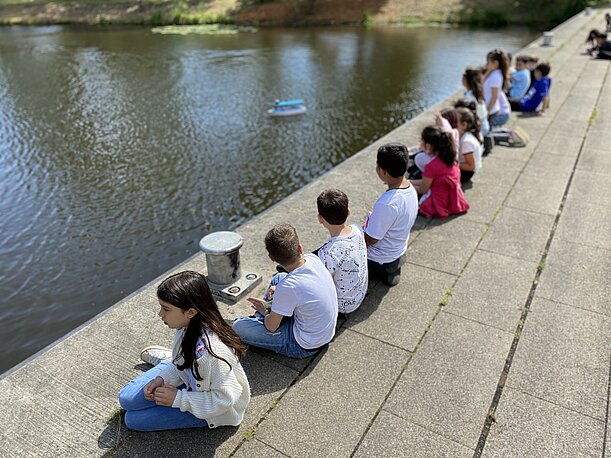 Kinder sitzen an der Kaimauer und beobachten ein ferngesteuertes Boot