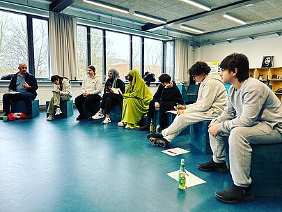 Schülerinnen und Schüler diskutieren mit Gästen im Sitzkreis im Forum