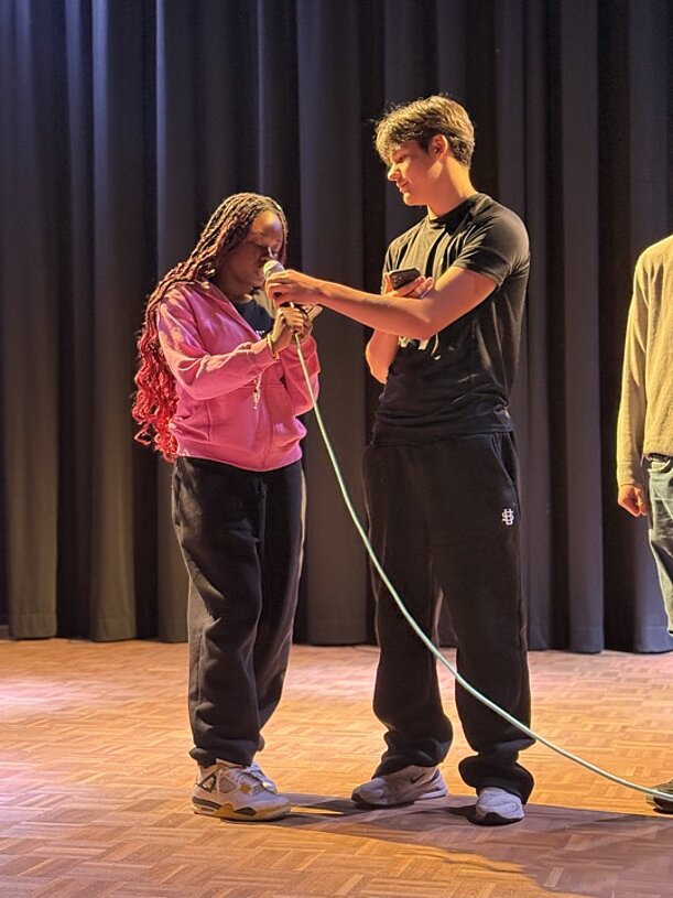 Schülerin und Schüler mit Mikrofonkabel auf der Bühne