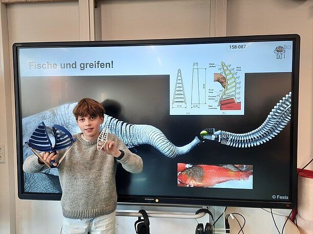 Karl Henri zeigt sein fertiges Modell vor der Folie „Fische und greifen!“