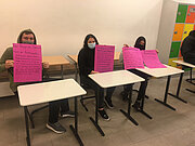 Drei Jugendliche der 10c halten an Schultischen pinke Plakate
