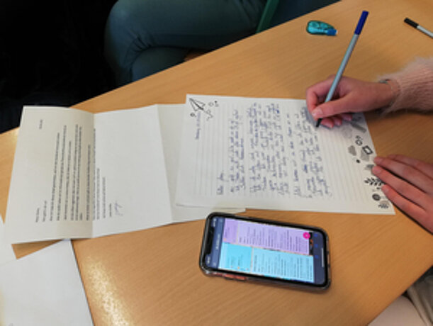 Handgeschriebener Brief auf einem Schultisch, daneben ein Smartphone