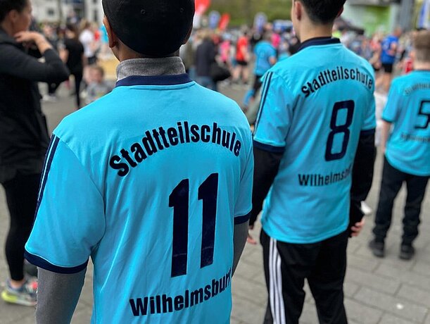 Zwei Läufer von hinten in türkisen Trikots „Stadtteilschule Wilhelmsburg“
