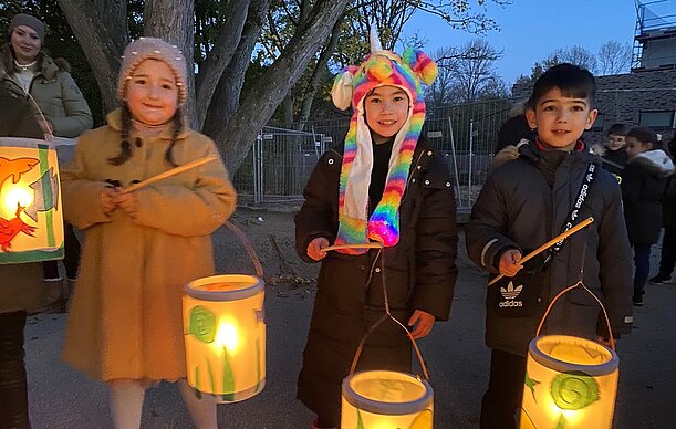 Drei Grundschulkinder zeigen stolz ihre leuchtenden Laternen