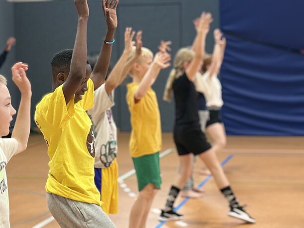 Kinder in gelben T-Shirts tanzen in der Sporthalle mit der NAFSI-Gruppe