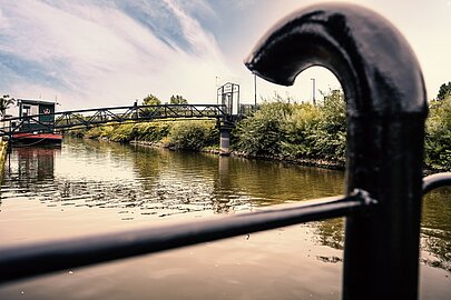 Schwarzes Geländer am Spreehafen mit Blick auf Brücke und grünes Ufer