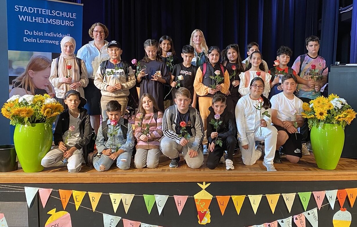 Klasse 5f mit Lehrerinnen und Rosen auf der Bühne bei der Einschulung