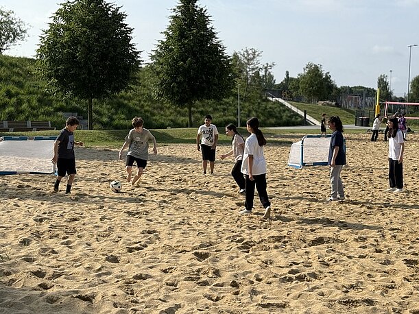 Jugendliche spielen Fußball im Sand beim Sporttag im Park