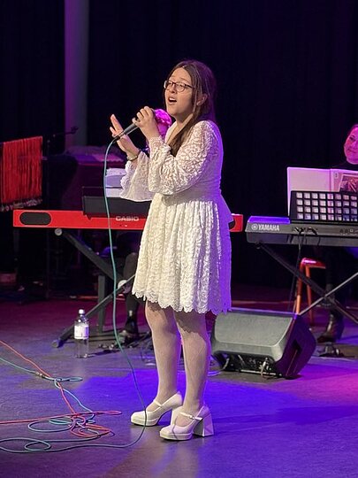 Sängerin im weißen Kleid singt auf der Bühne der Aula