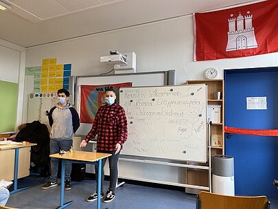 Schüler am Tisch vor Hamburg-Flagge und Whiteboard bei der Eröffnung