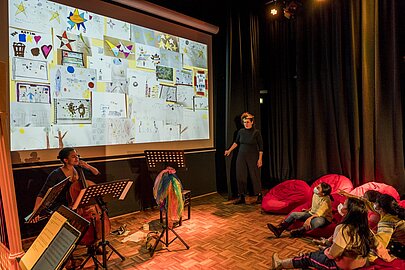Cellistin spielt vor Leinwand mit Kinderzeichnungen beim Konzert in der Aula