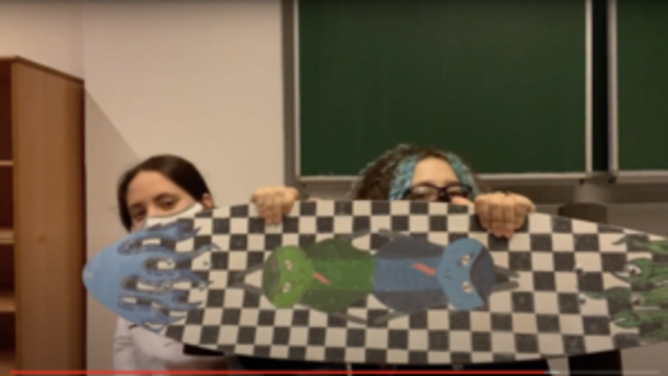 Zwei Schülerinnen halten ein Longboard mit Schachbrettmuster hoch