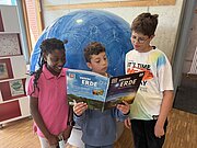 Drei Kinder lesen das Heft „Unsere Erde“ vor einem großen Globus