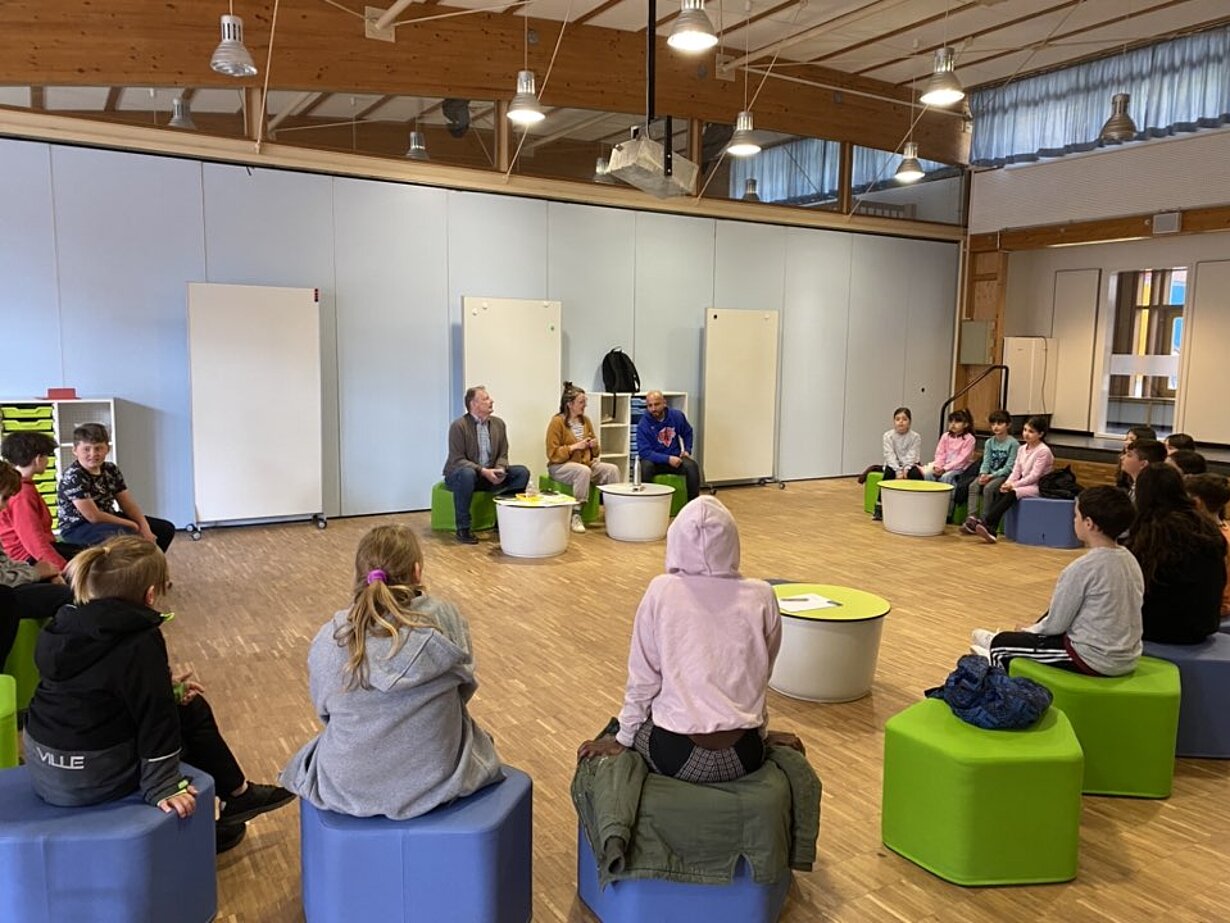 Kinderkonferenz im Sitzkreis auf bunten Hockern in der Grundschule