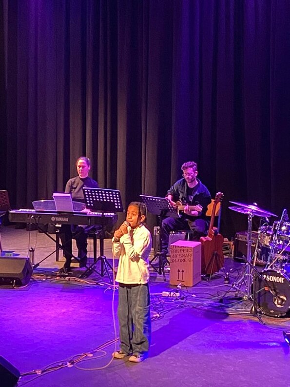 Sandro singt mit Mikrofon vor der Live-Band auf der Aulabühne