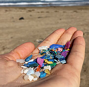 Hand mit bunten Mikroplastikteilchen am Strand