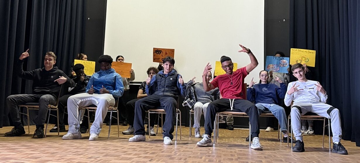 Profilgruppe Kultur, Movement und Bühne der 8d bei einer Präsentation auf Stühlen