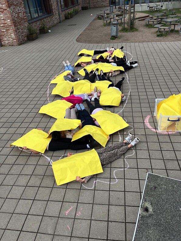 Schülerinnen und Schüler formen ein Seepferdchen aus gelben Tüchern