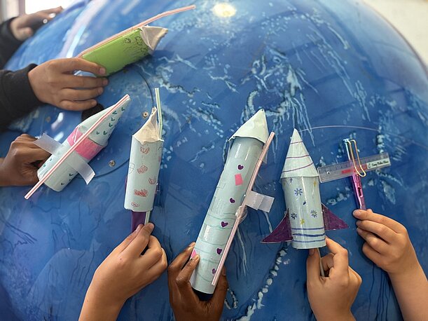 Kinderhände halten gebastelte Papierraketen an einen Globus