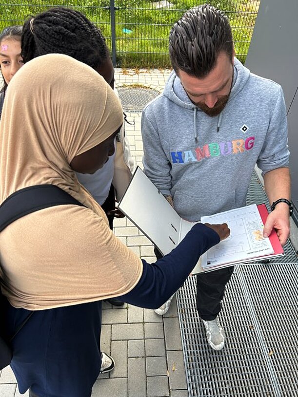 Schülerin unterschreibt auf einem Klemmbrett bei einem Betreuer