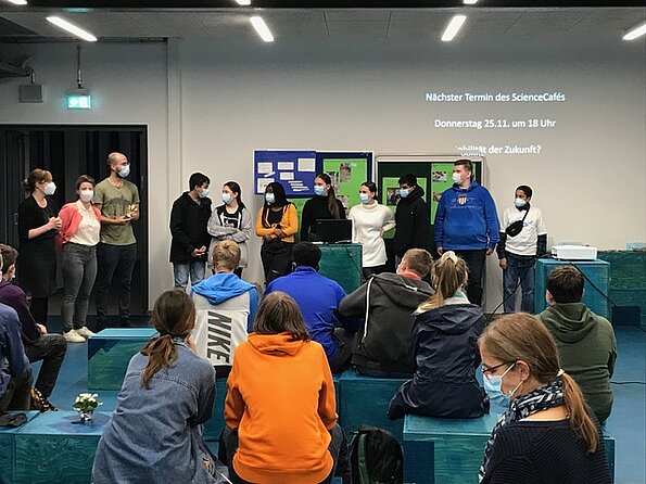 Gäste im ScienceCafé sitzen vor Leinwand und Stellwänden