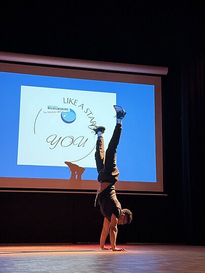 Handstand auf der Bühne vor Leinwand mit Schriftzug „Like a Star – You“